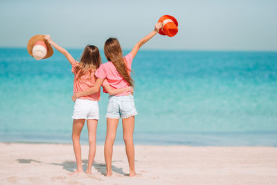 Rear view of women standing at beach against sky