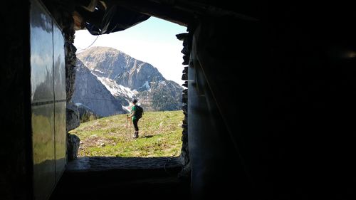 Side view of female hiker standing on field against rocky mountain