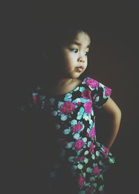 Girl looking away while standing against black background