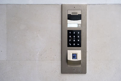 Matte metal intercom call panel with white digital buttons and fingerprint scanner on limestone wall