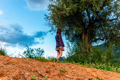 Woman standing by tree on field against sky