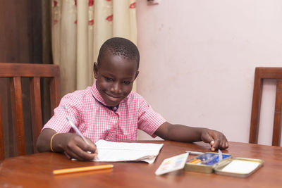 Portrait of young african schoolboy focused smiling writing on paper