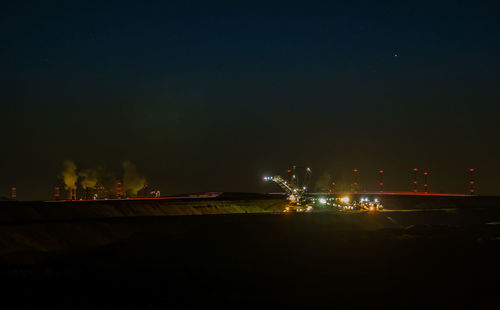 Illuminated city by river against sky at night