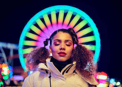 Smiling woman standing against illuminated ferris wheel at night