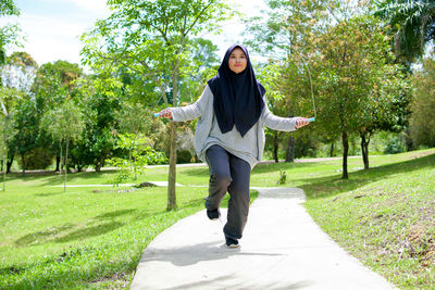 Full length portrait of smiling young woman in park