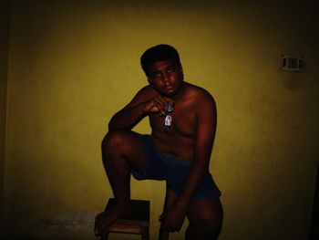 Portrait of young man sitting against wall