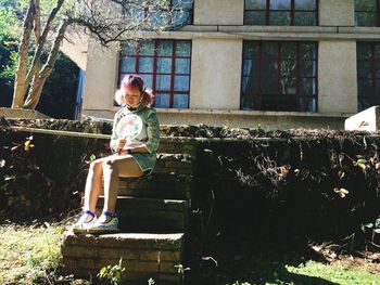 Side view of woman sitting against building