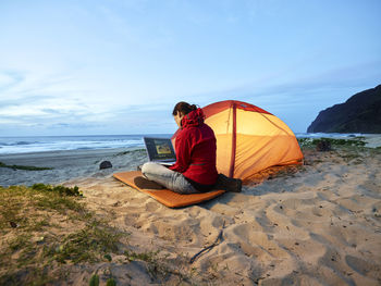 Usa, hawaii, kauai, polihale state park, woman using laptop at tent on the beach at dusk