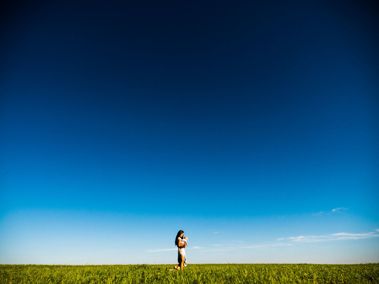 REAR VIEW OF MAN STANDING ON GRASSY FIELD AGAINST CLEAR SKY