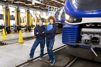 Smiling engineer holding file folder standing by colleague in factory