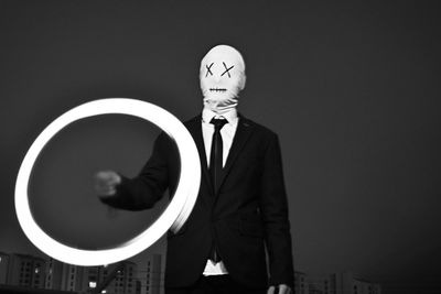 Businessman wearing mask making light painting against clear sky at night