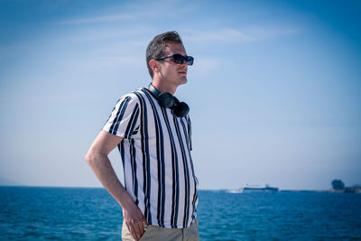 Young man wearing sunglasses standing by sea against sky