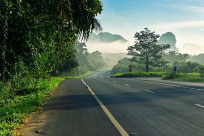 Empty road by trees against sky