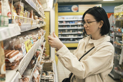 A woman in a grocery supermarket chooses food and carefully reads the composition of the products. 