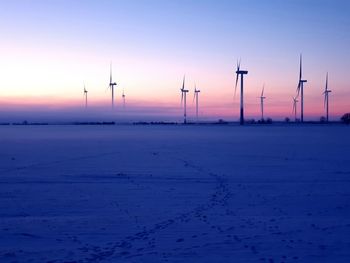 Wind turbines on field against sky during sunset