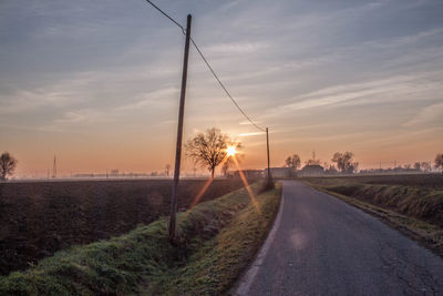 Empty road amidst field against sky during sunset