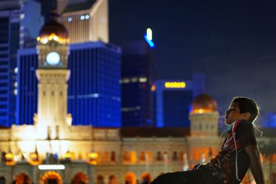 Side view of woman looking at illuminated city at night