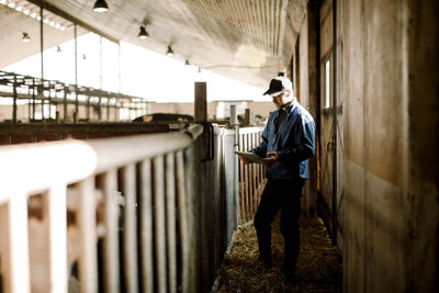 Farmer using digital tablet standing by railing at dairy farm