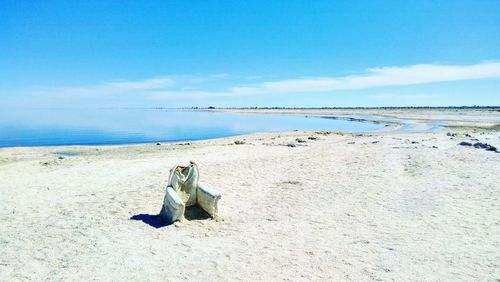 A battered and weather worn armchair sits lonely on beach of salton sea against blue sky