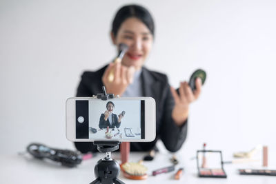 Young woman blogging through smart phone while holding beauty products