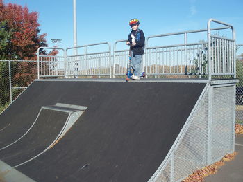 Boy standing with push scooter on ramp at skateboard park