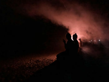 Silhouette people against illuminated sky at night