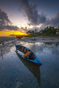 Boat moored on beach against sky during sunset