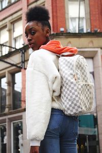 Portrait of woman wearing backpack while standing in city