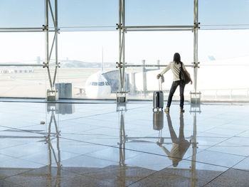 Young woman standing with baggage near the airport window waiting for the flight