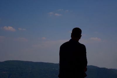 Rear view of silhouette man standing on mountain against sky