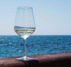 Glass of water on table by sea against sky