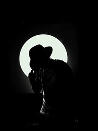 Silhouette man sitting against black background