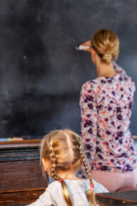 Rear view of teacher teaching female student in classroom