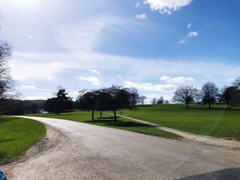 Empty road by trees on field against sky