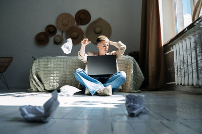 Woman professional content writer working with papers and laptop computer at home while sitting on