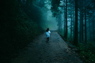 Rear view of woman walking on footpath in forest