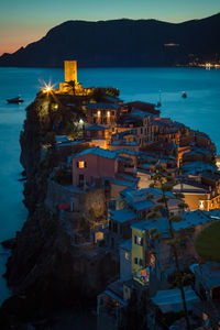 Illuminated town by sea against sky at night