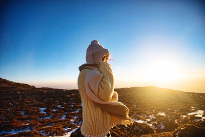 Woman standing on rock against sky during sunset