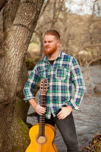 Full length of man playing guitar on tree trunk