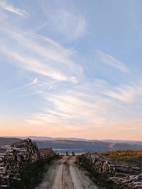 People standing on road by river against sky during sunset