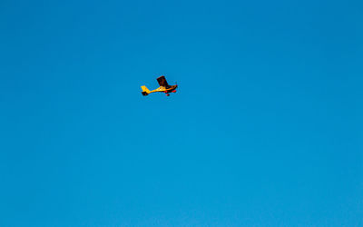 Low angle view of airplane flying against clear blue sky