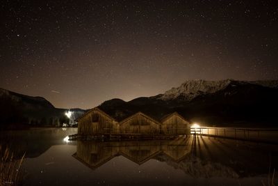 Illuminated buildings by lake against sky at night