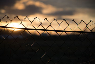 Close-up of chainlink fence against sky during sunset