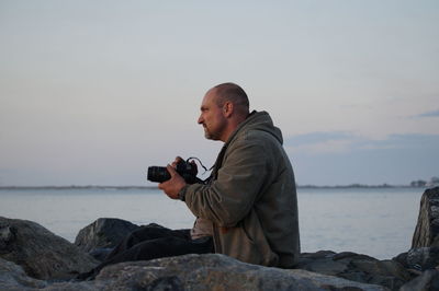 Man photographing on rock by sea against sky