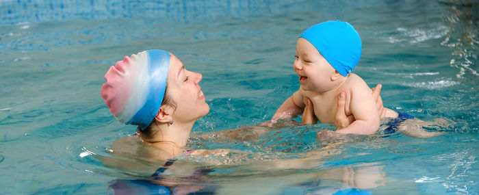 Early age swimming in pool. baby boy trained to swim in water. happy child with trainer woman in