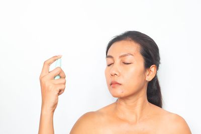 Portrait of shirtless young woman using smart phone against white background