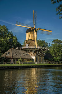 Traditional windmill by lake against sky