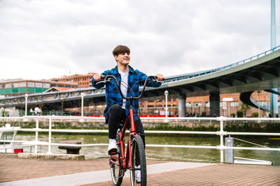 Man riding bicycle on bridge against sky