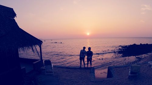 People standing on beach against sky during sunset