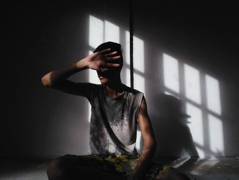 Young sad man hiding face while sitting against wall in room